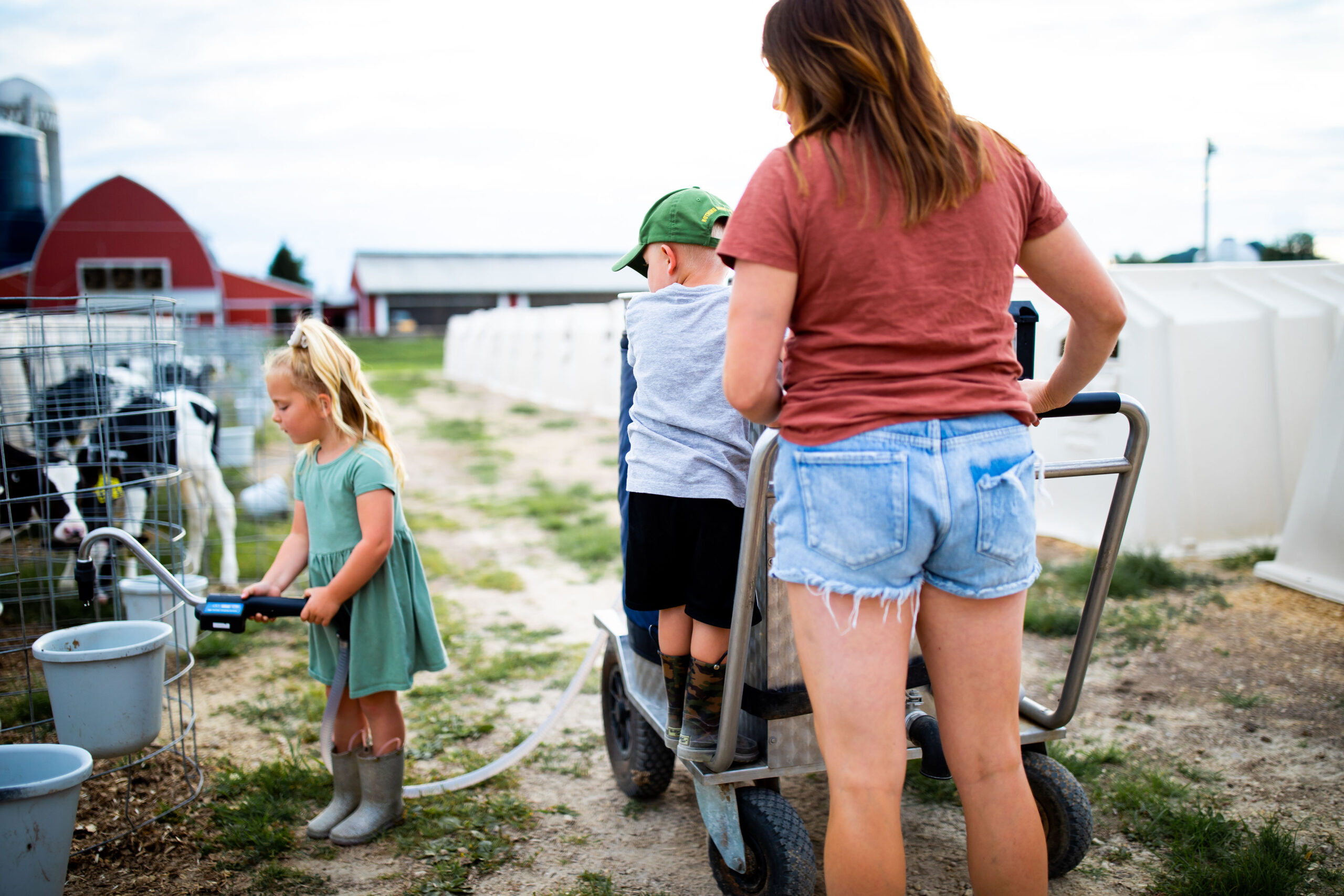 Wisconsin dairy farmer mom with her kids feeding calves with a milk taxi