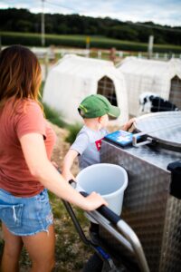 Wisconsin female dairy farmer and son feeding calves with a milk taxi