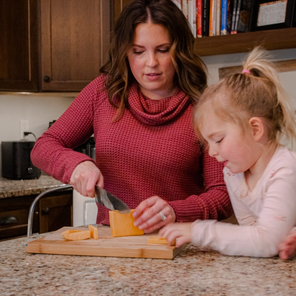 modern day farm chick Annaliese Wegner and her daughter cooking and cutting cheese